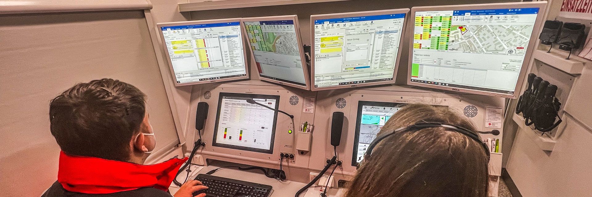 Foto: Zwei Einsatzkräfte sitzen an den Funkarbeitenplätzen im Einsatzleitwagen